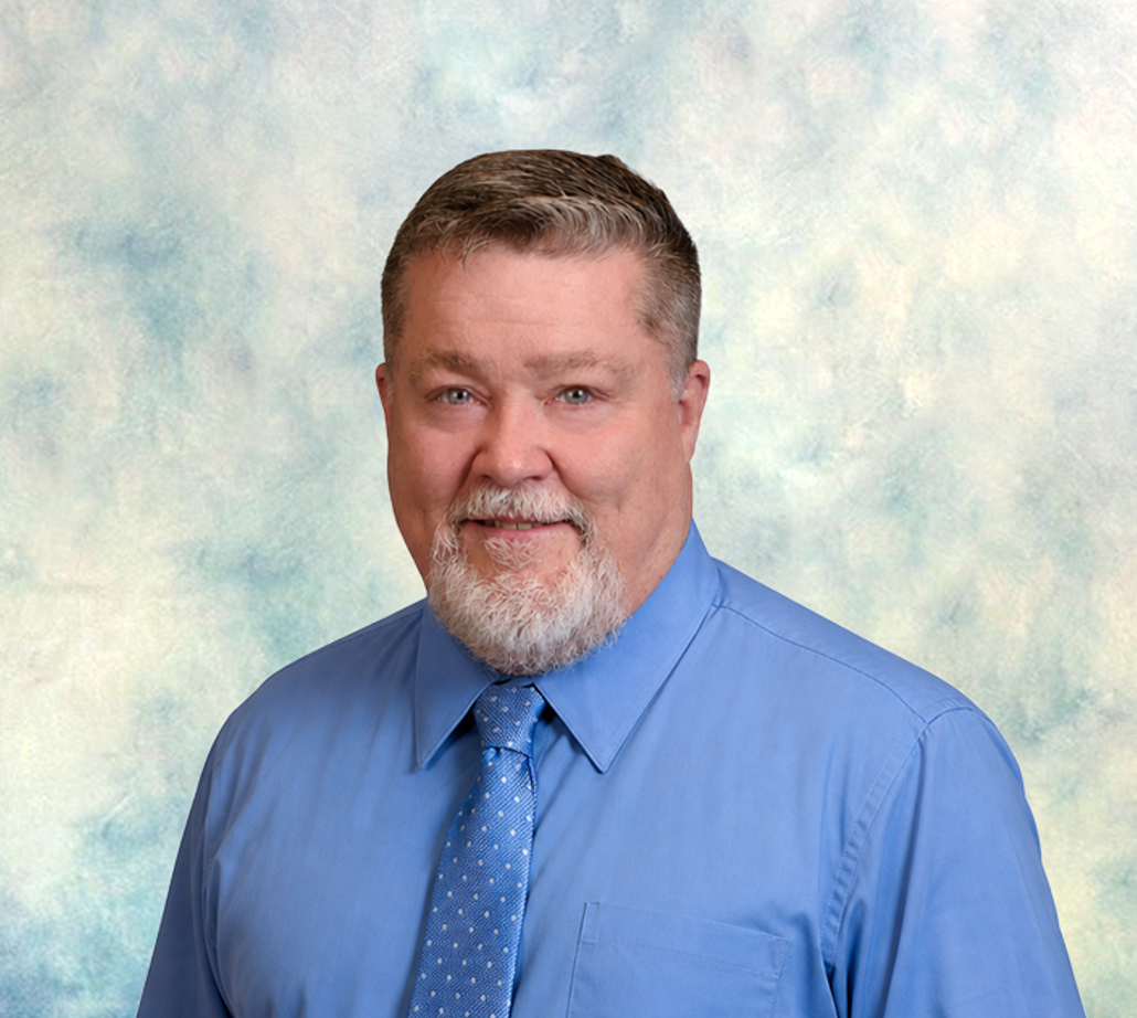 Portrait of a smiling man in a blue shirt and tie against a soft studio backdrop