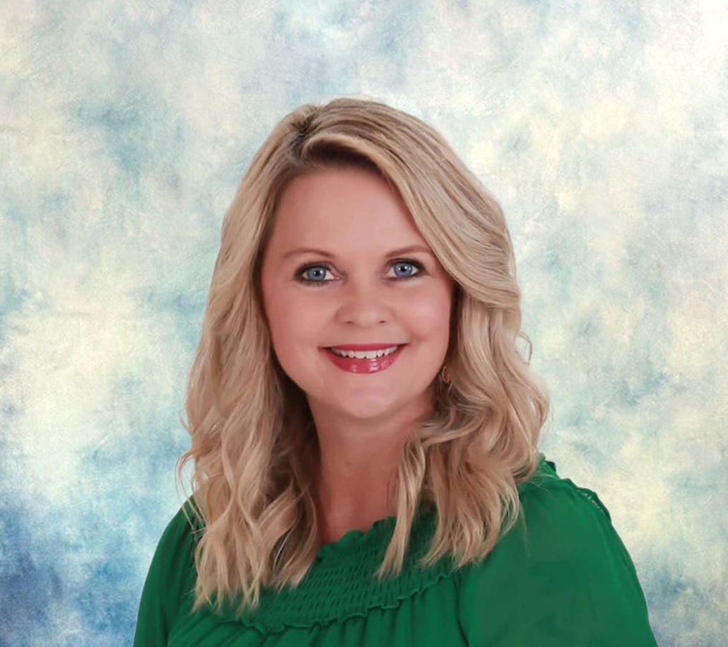 Smiling blonde woman in a green blouse against a soft blue studio backdrop