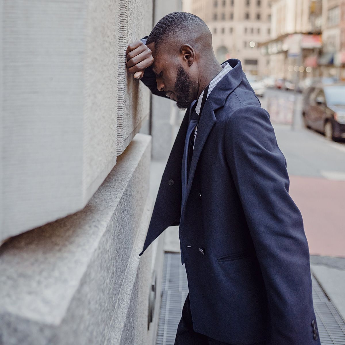 business man in suit with face on arm leaning against a building after being laid off from job