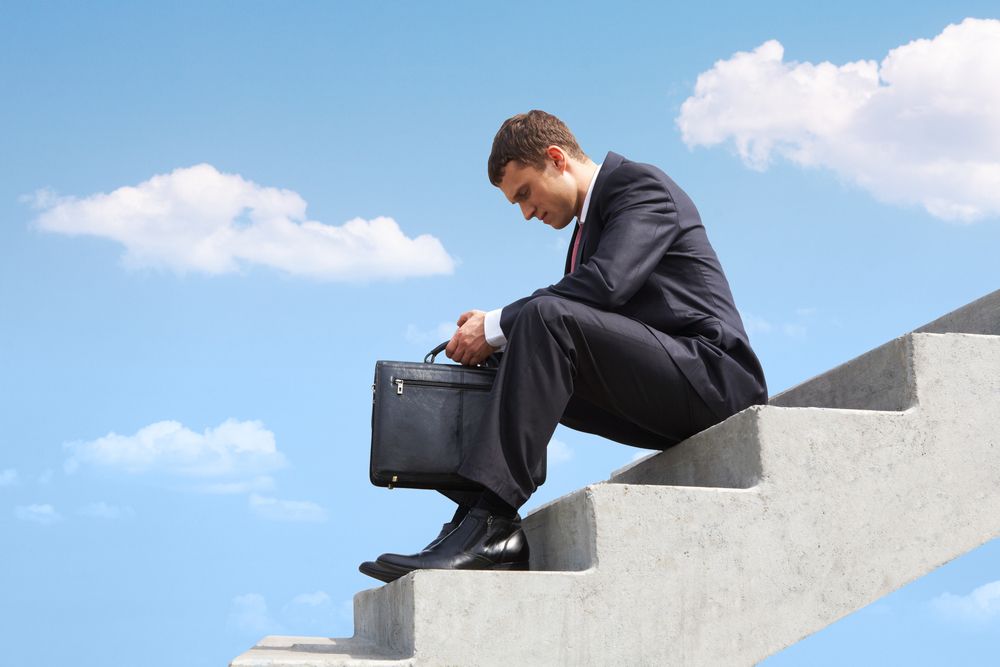 vice president of company sitting on stairs looking down at feet because he's stuck in his role