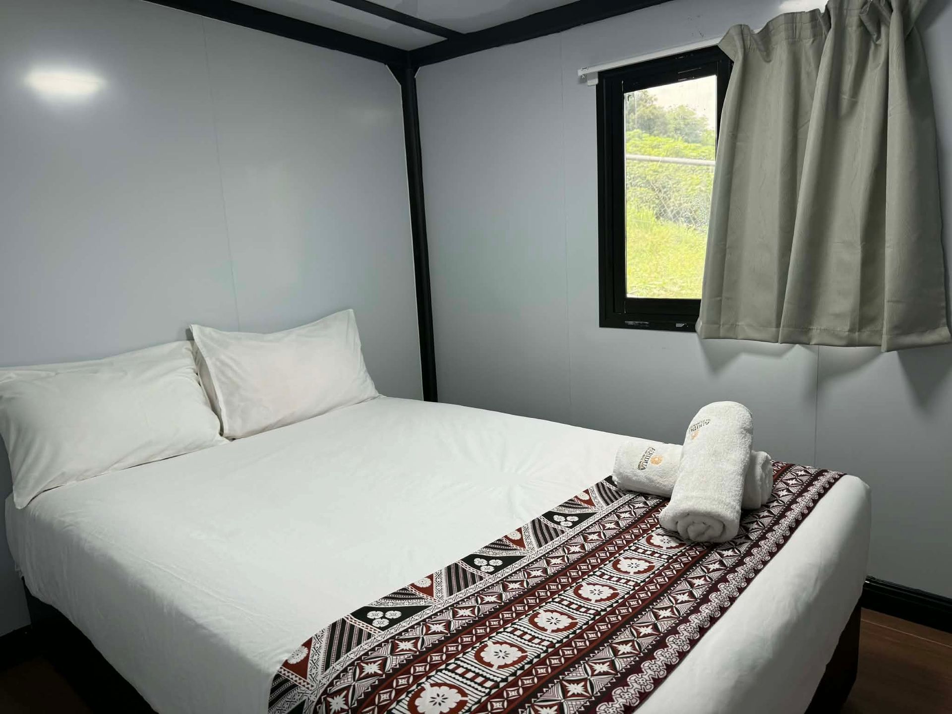 Small bedroom with a white bed, patterned throw, and window with curtains