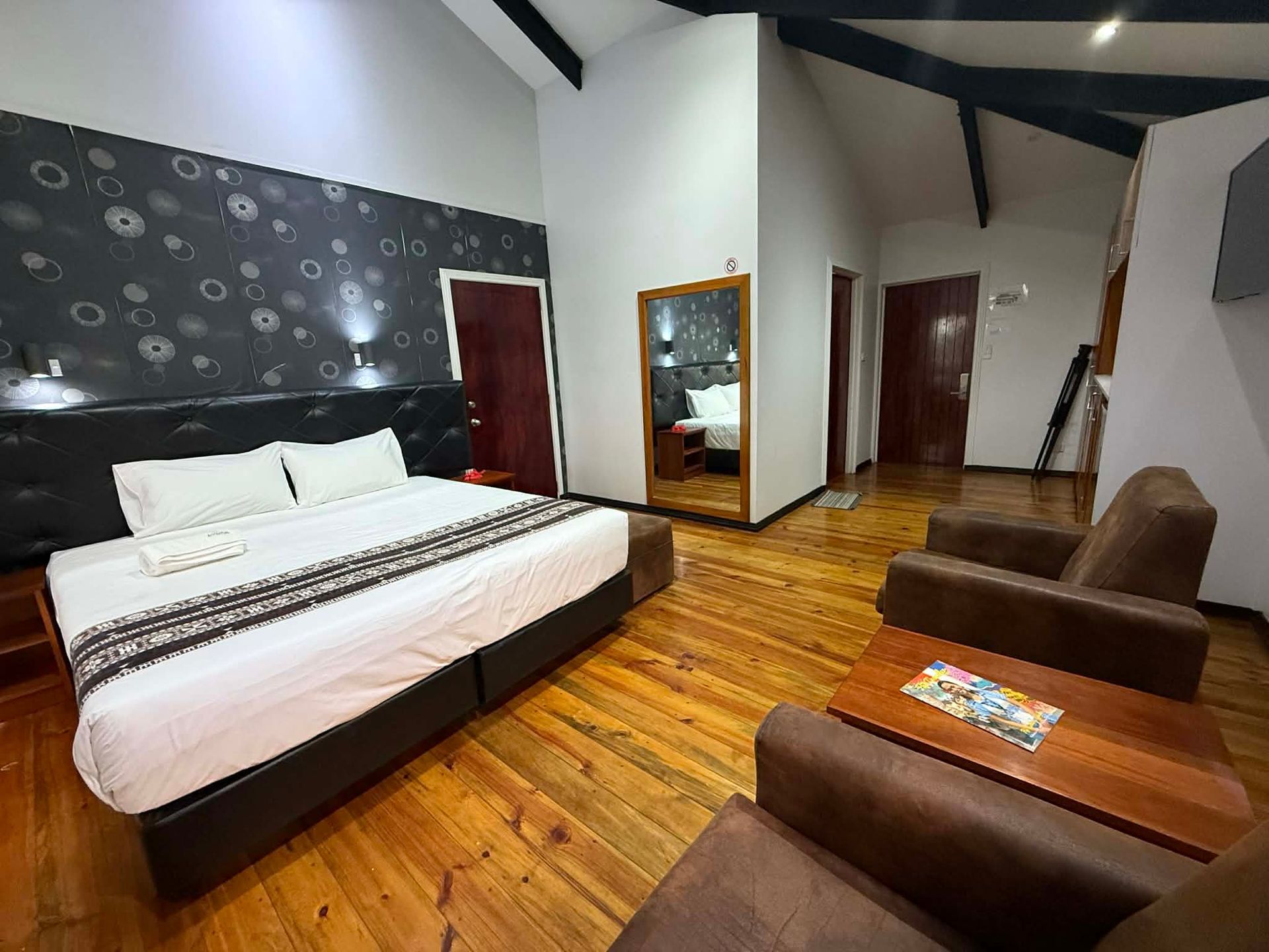 Modern bedroom with a bed, sofa, wooden floor, mirror, and red doors