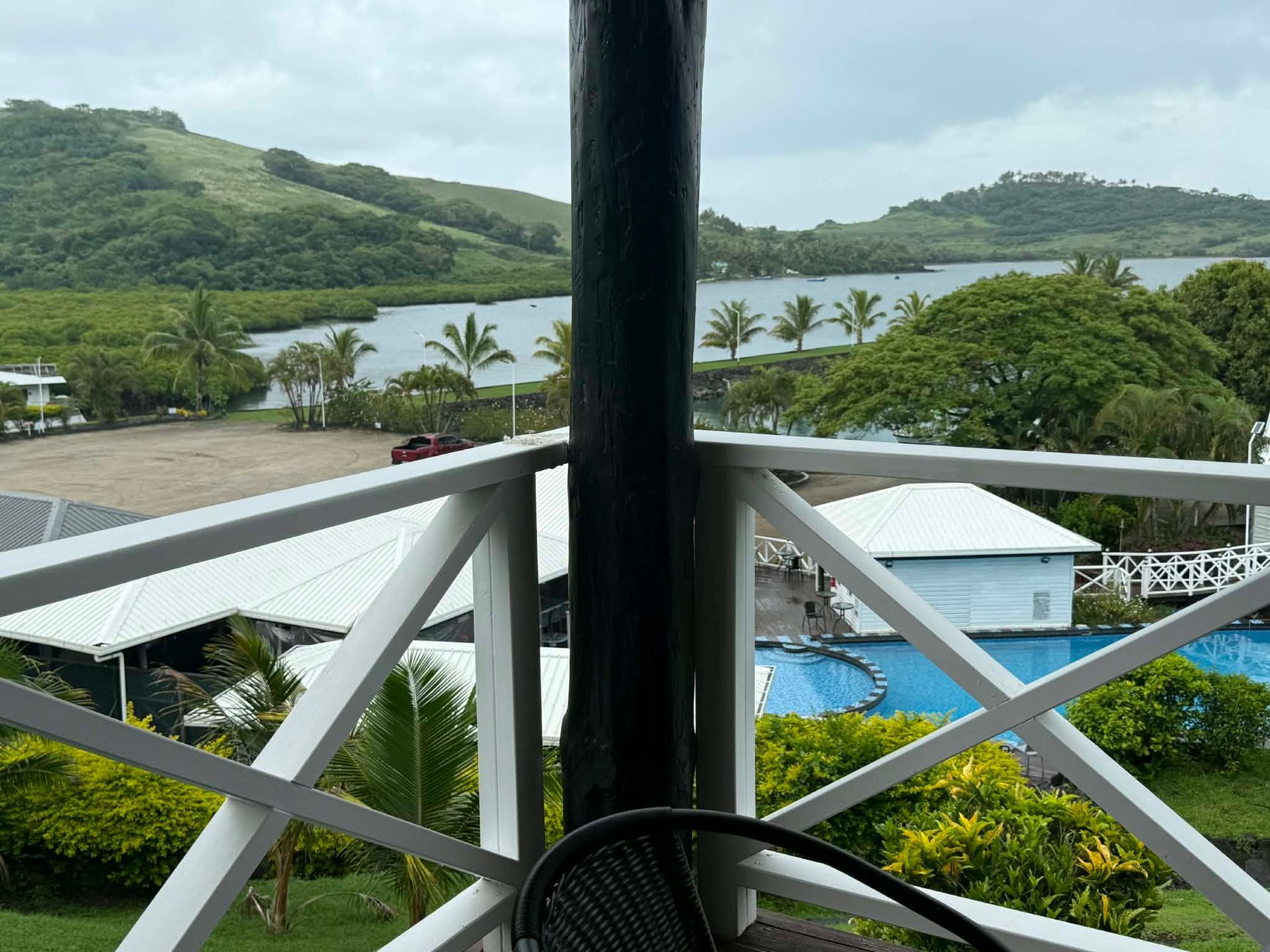 Balcony view of a tropical bay with green hills, white railings, and a pool below