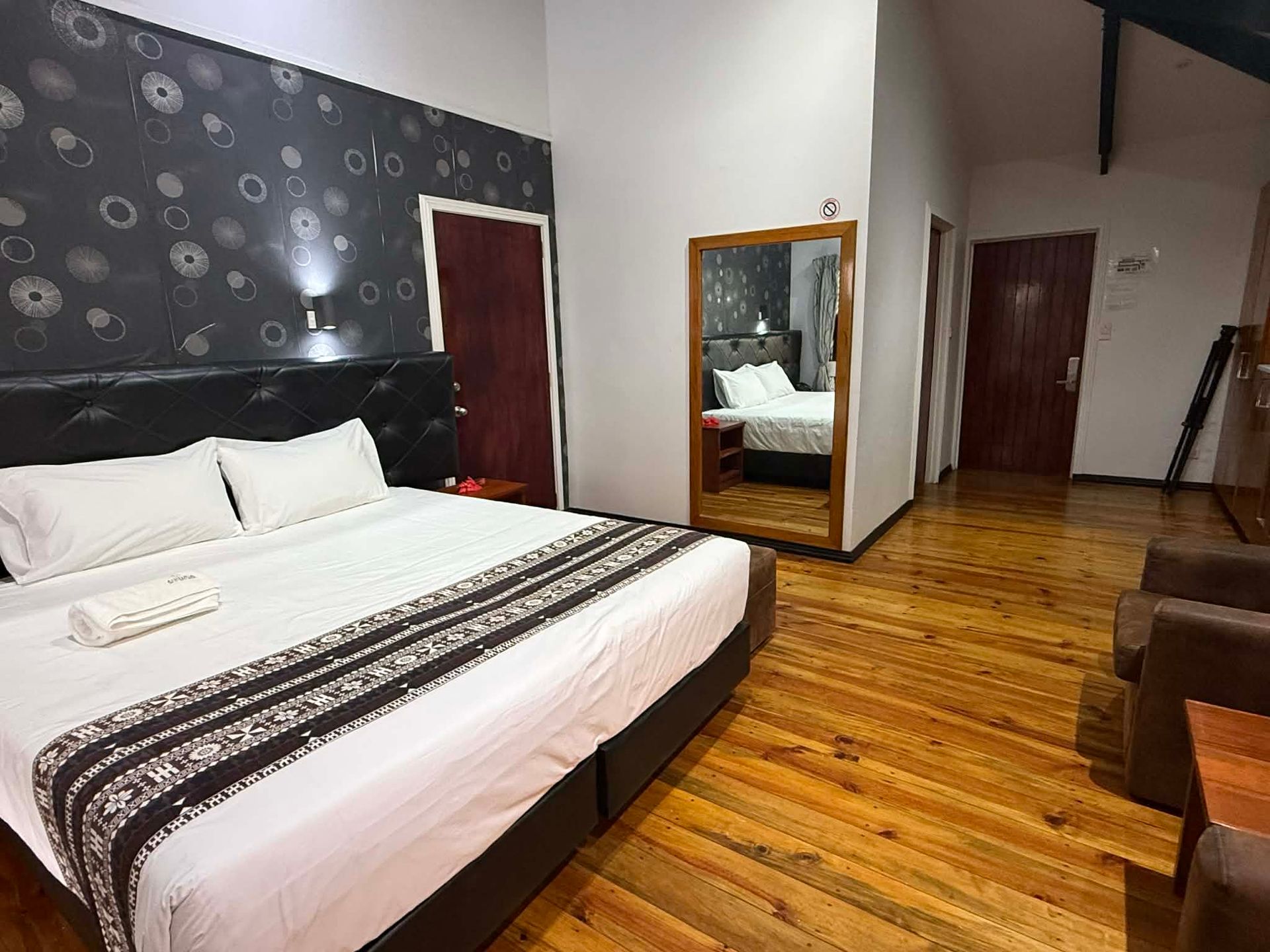Modern bedroom with a large bed, wood floors, mirrored dresser, and dark accent wall.