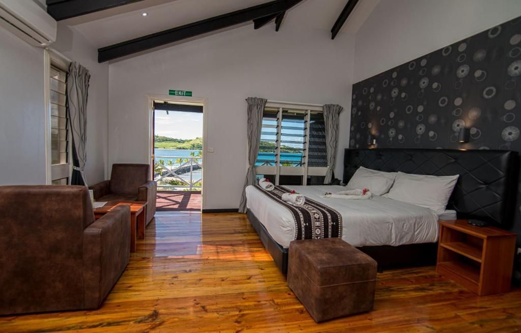 Cozy bedroom with wooden floor, bed, brown sofa, and open door to a balcony with ocean view