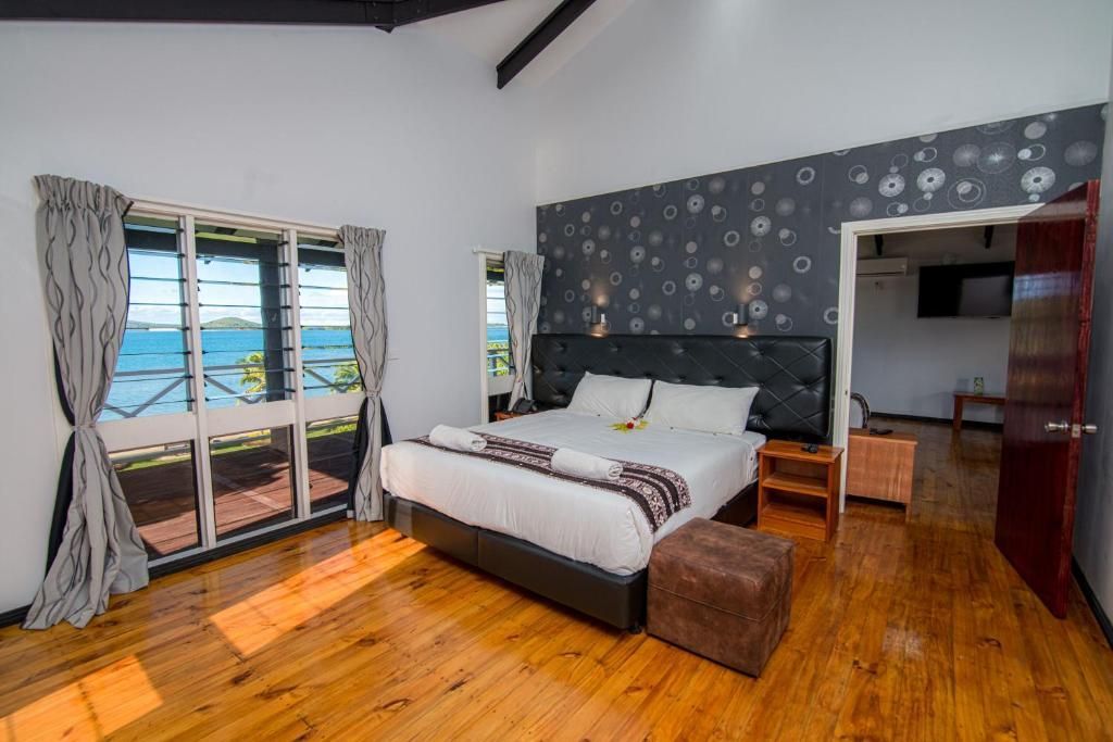 Spacious bedroom with a king bed, wooden floor, patterned accent wall, and ocean view through large windows