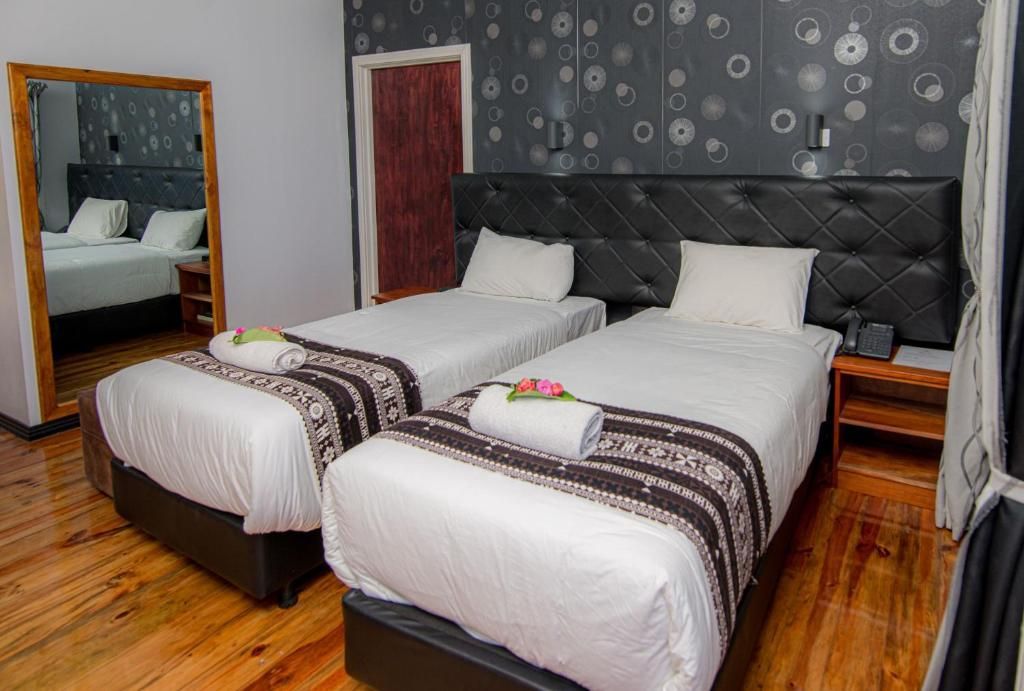 Hotel room with two white beds, dark headboard, wooden floor, and a large mirror wardrobe