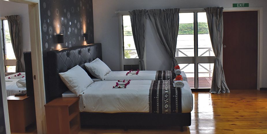 Modern bedroom with a large bed, gray curtains, wood floor, and sliding doors opening to a balcony.