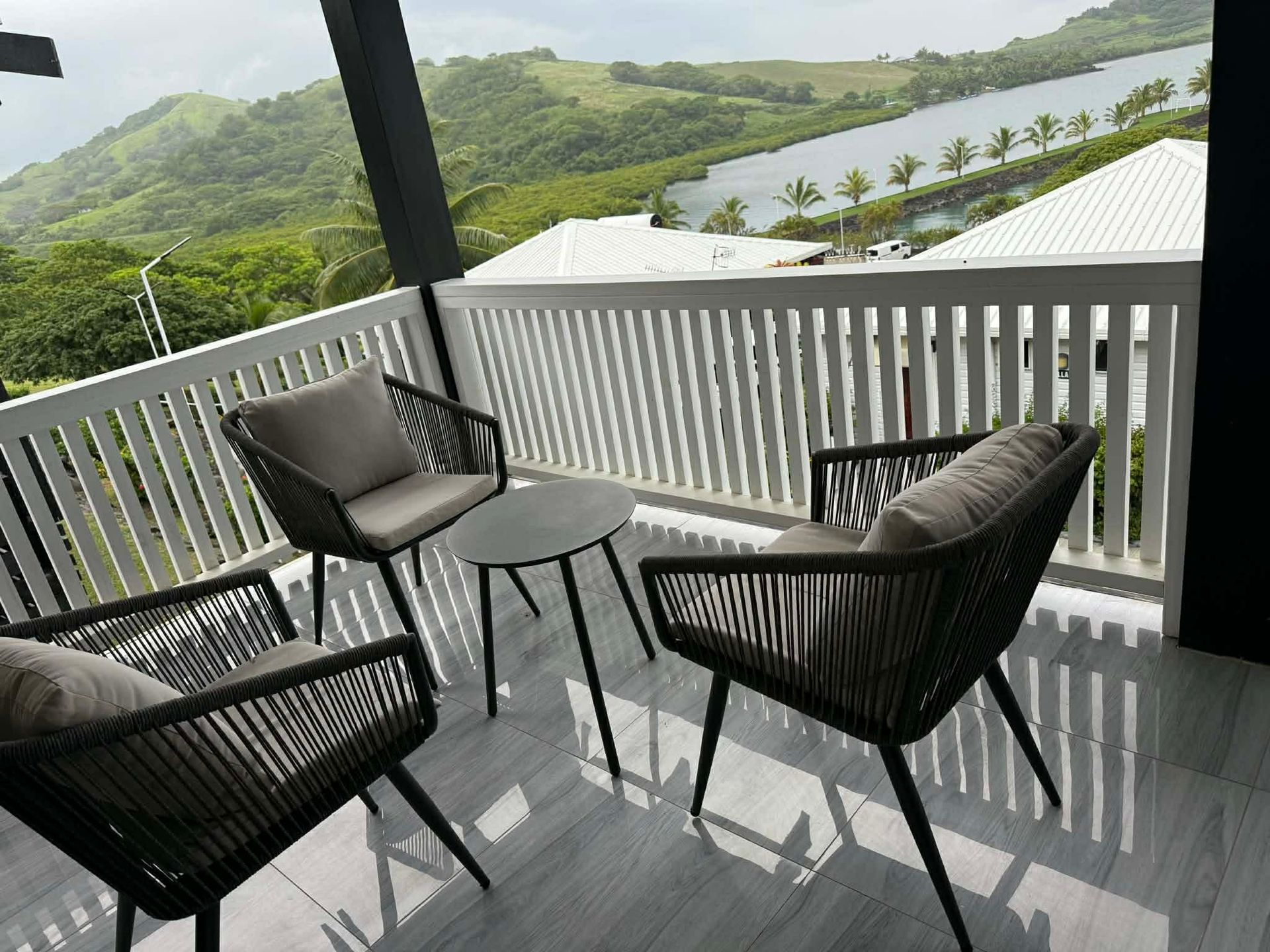 Balcony with black chairs and a table overlooking green hills and a river.