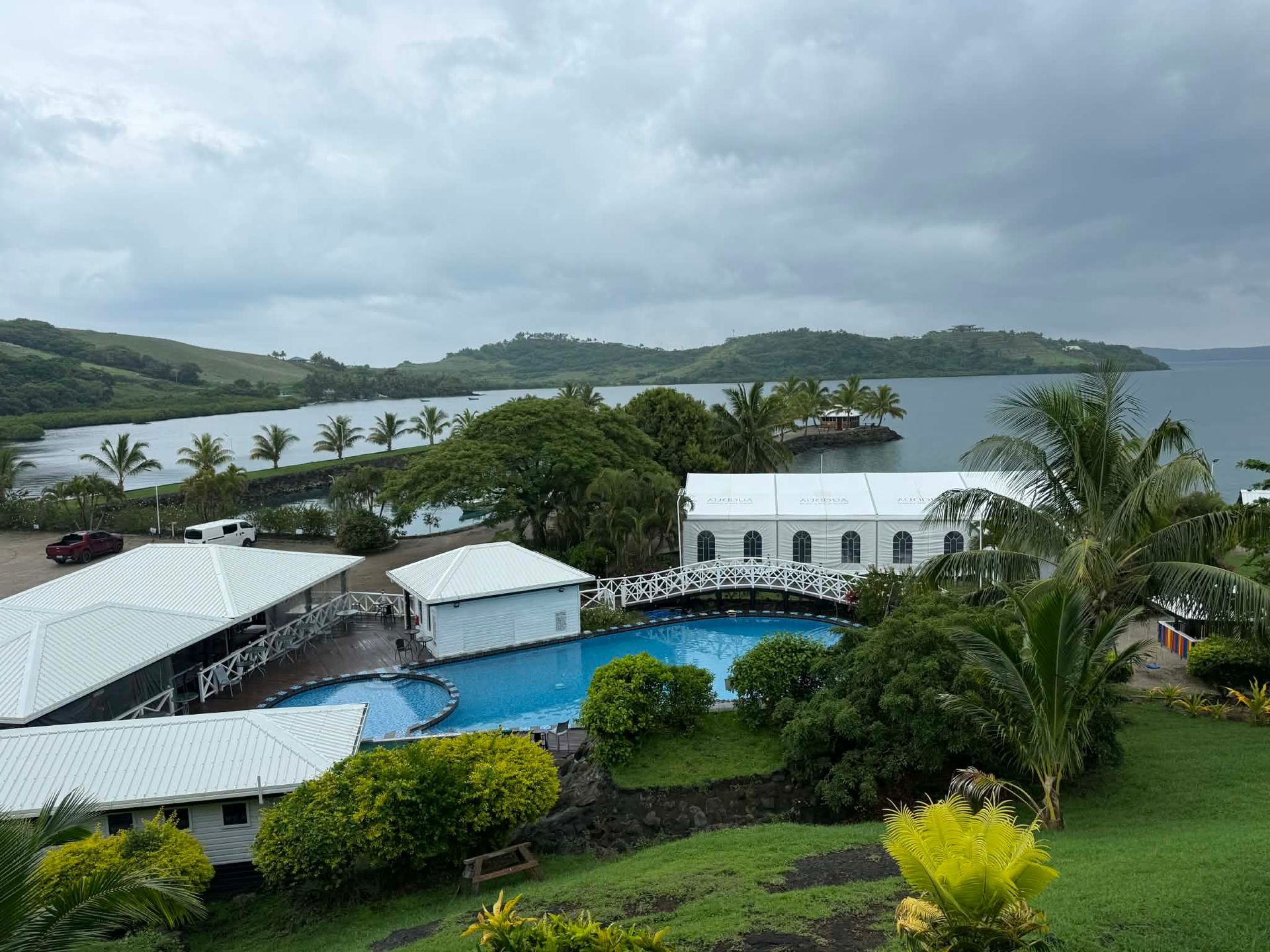 Resort pool and white buildings overlooking a tropical bay under cloudy skies