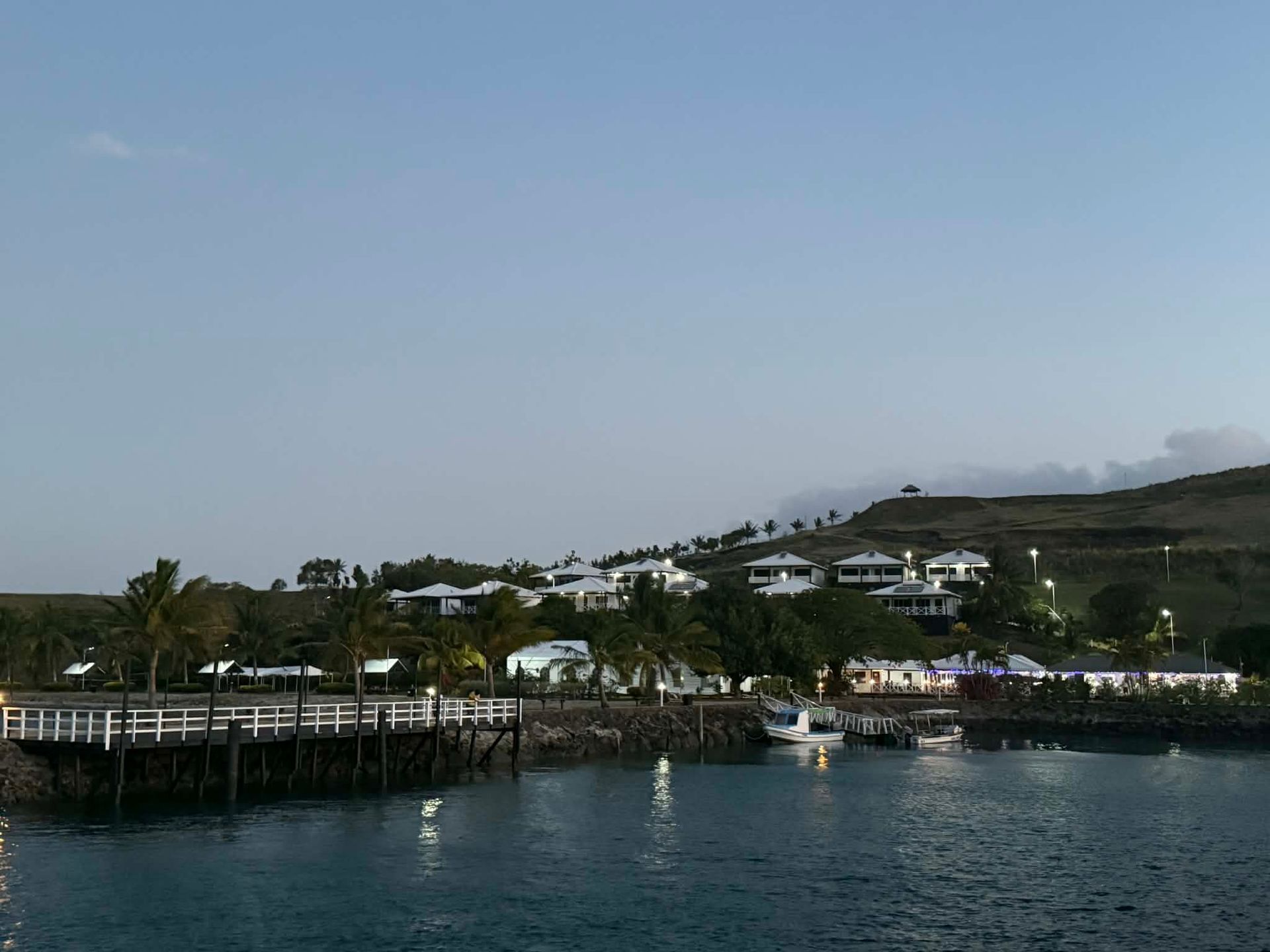 Harbor with white buildings on a hillside, wooden pier, and calm blue water under a clear sky