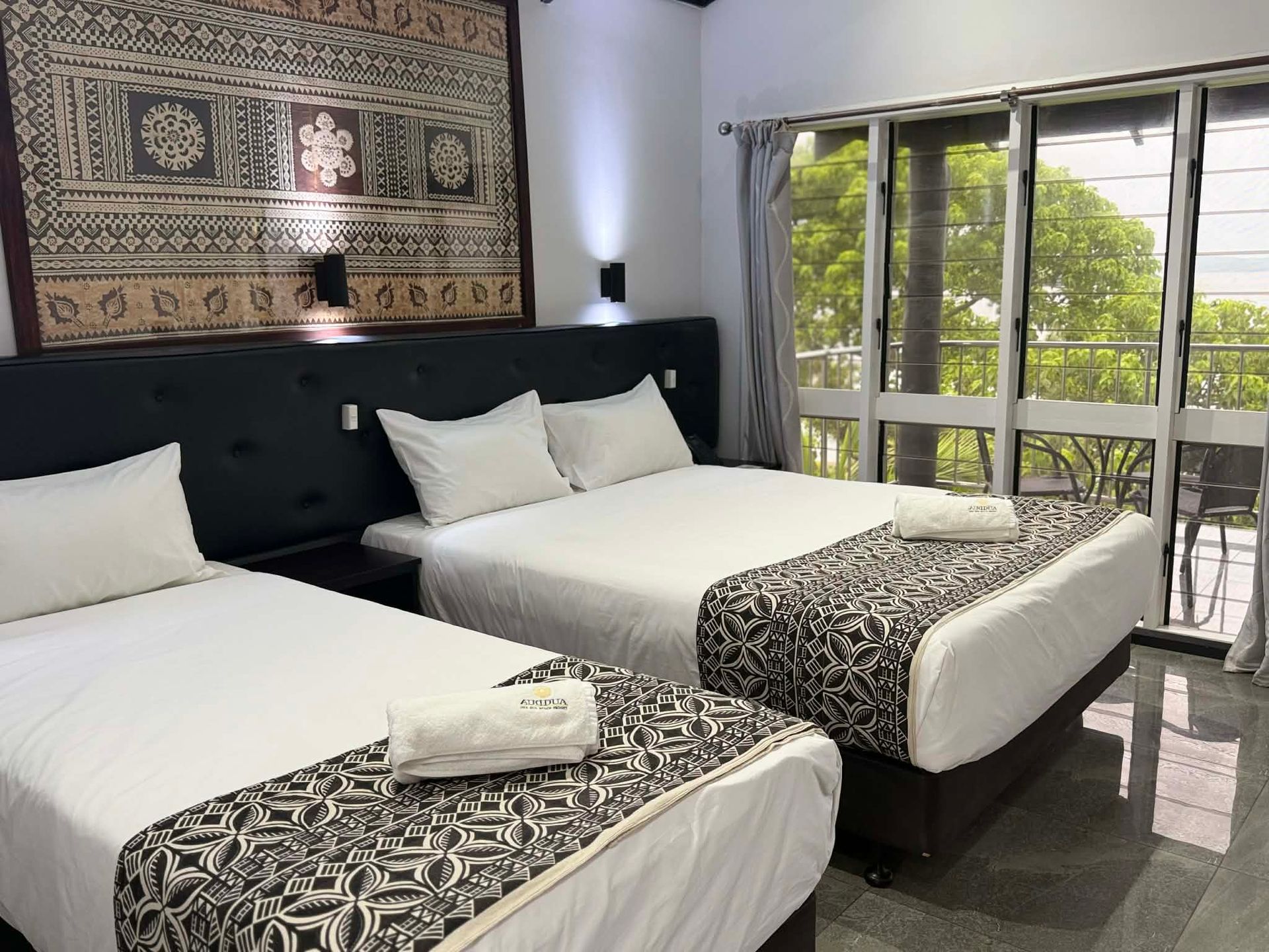 Bright hotel room with two twin beds, patterned bedding, and a balcony view of greenery