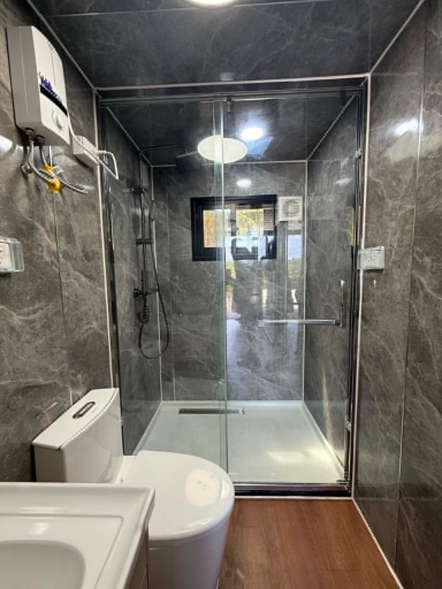 Modern bathroom with gray tile, white toilet and sink, and a glass-enclosed shower over a wood floor