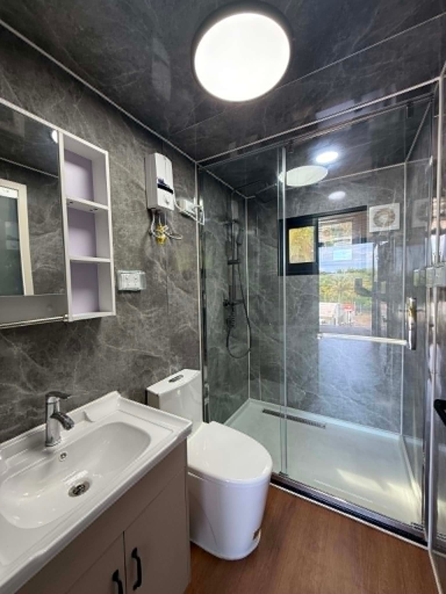 Modern bathroom with dark tile, white sink and toilet, and a glass shower enclosure.