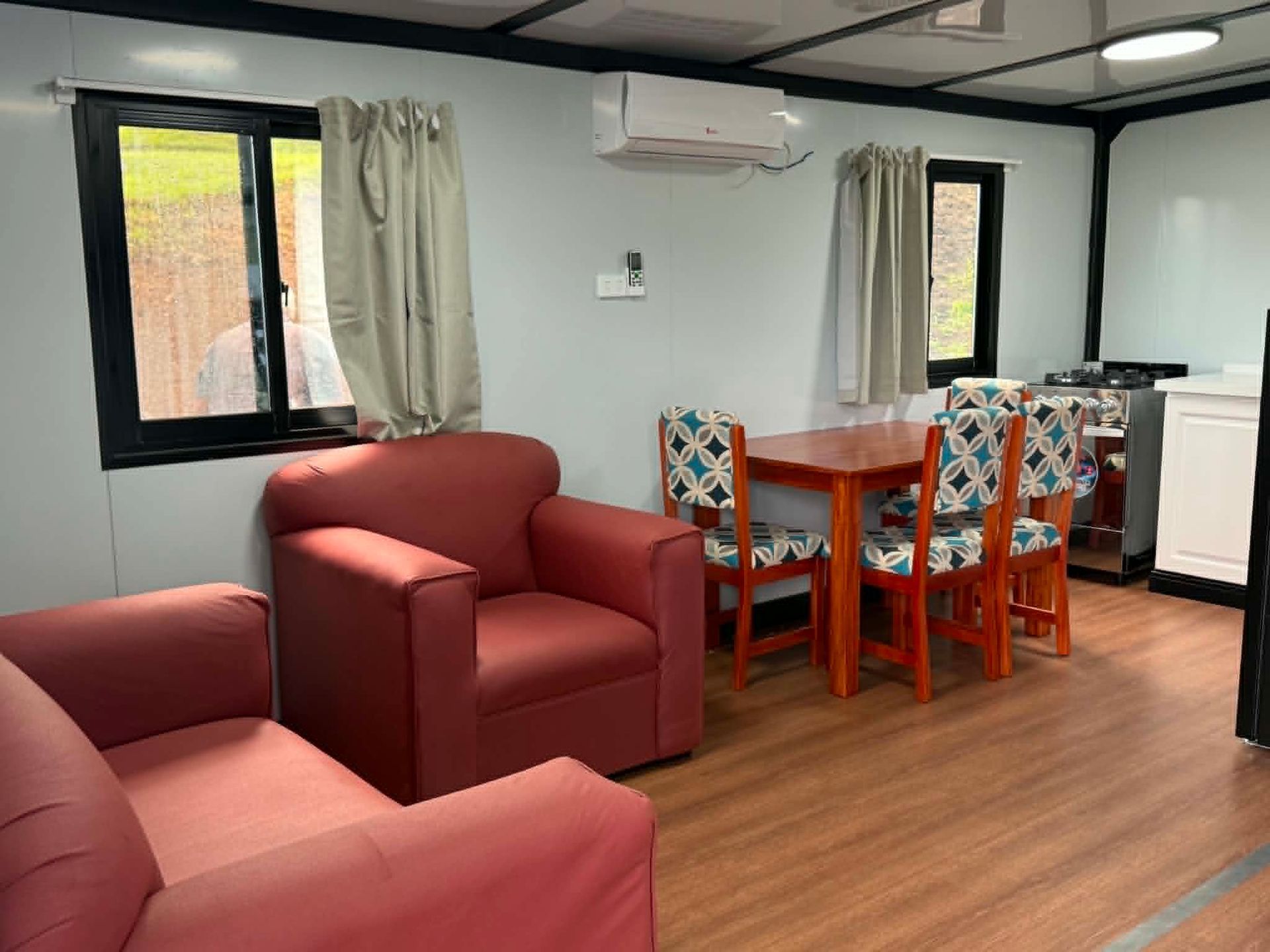 Small living-dining room with red chairs, orange table, wood floor, and curtained windows