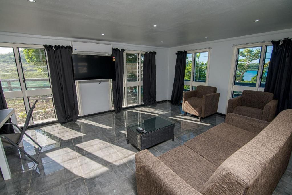 Modern living room with gray sofas, TV, coffee table, and large windows overlooking a bright outdoor view