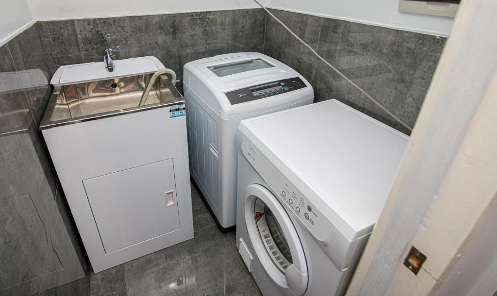 Small laundry room with a sink, washing machine, and dryer on gray tile flooring.