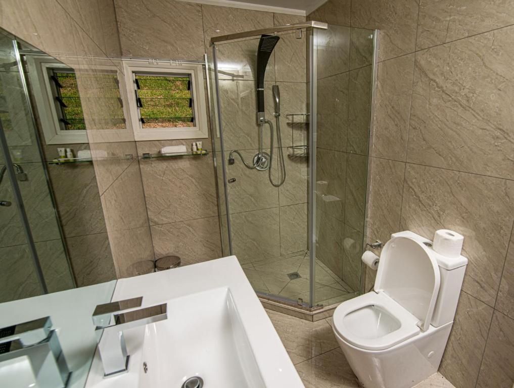 Modern beige bathroom with glass shower, white sink, and toilet with bidet spray.