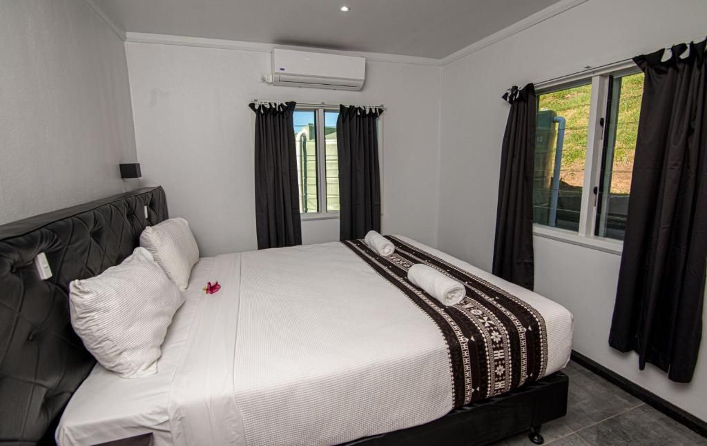 Modern bedroom with a large bed, black curtains, and bright windows