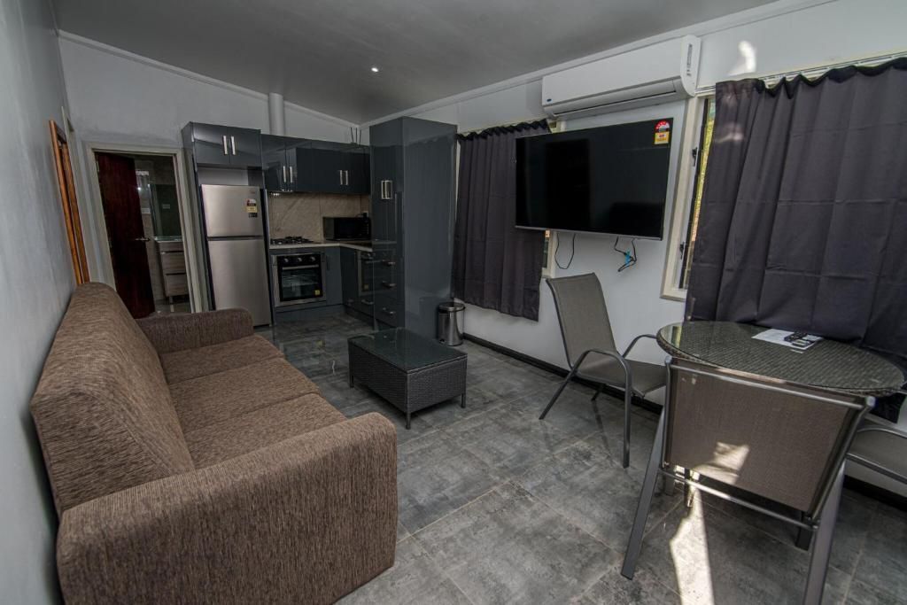 Small living room with brown sofa, TV, gray curtains, and a dining table by a window.