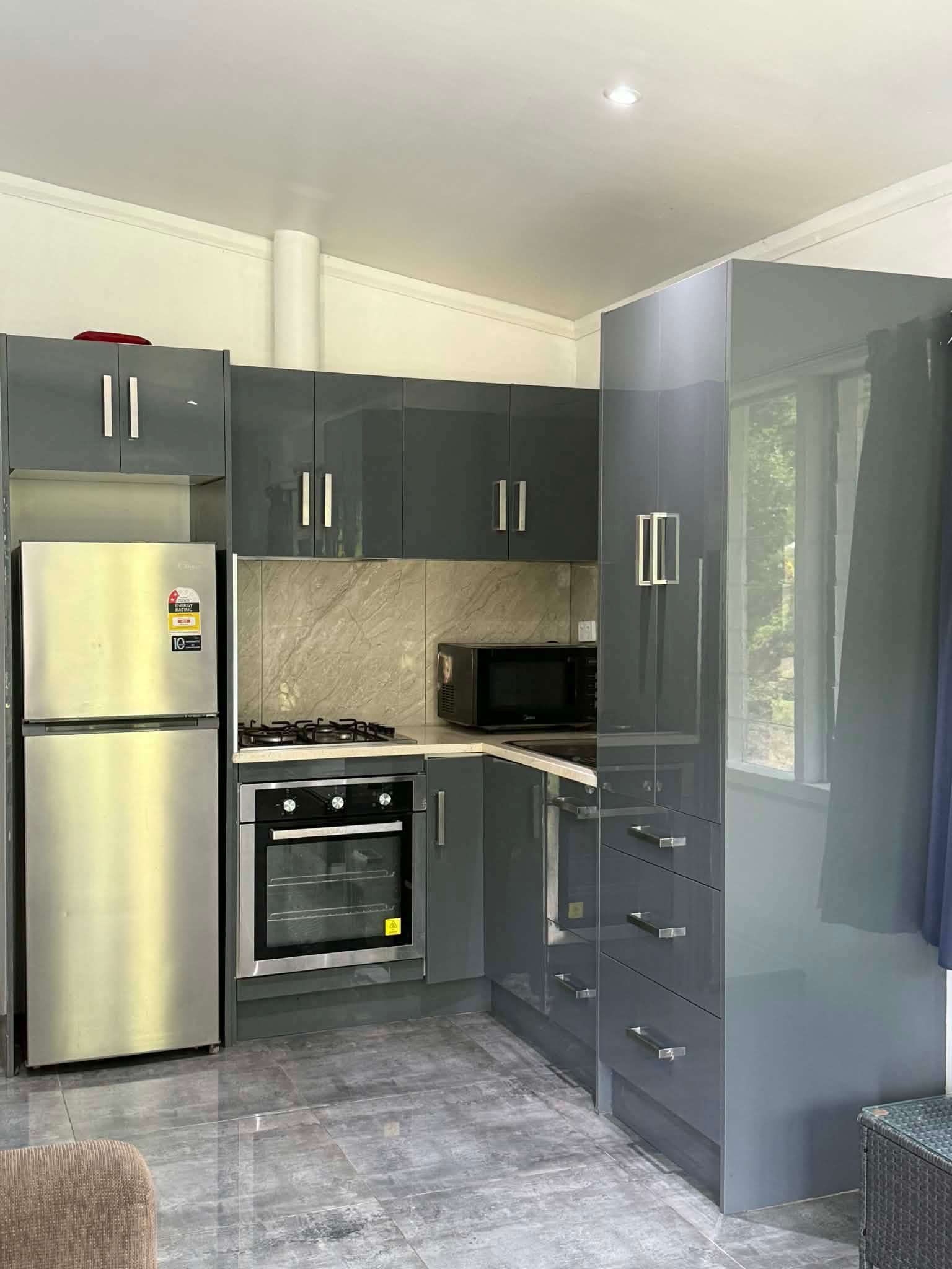 Modern kitchen with dark gray cabinets, stainless fridge, built-in oven, and glossy tiled floor.