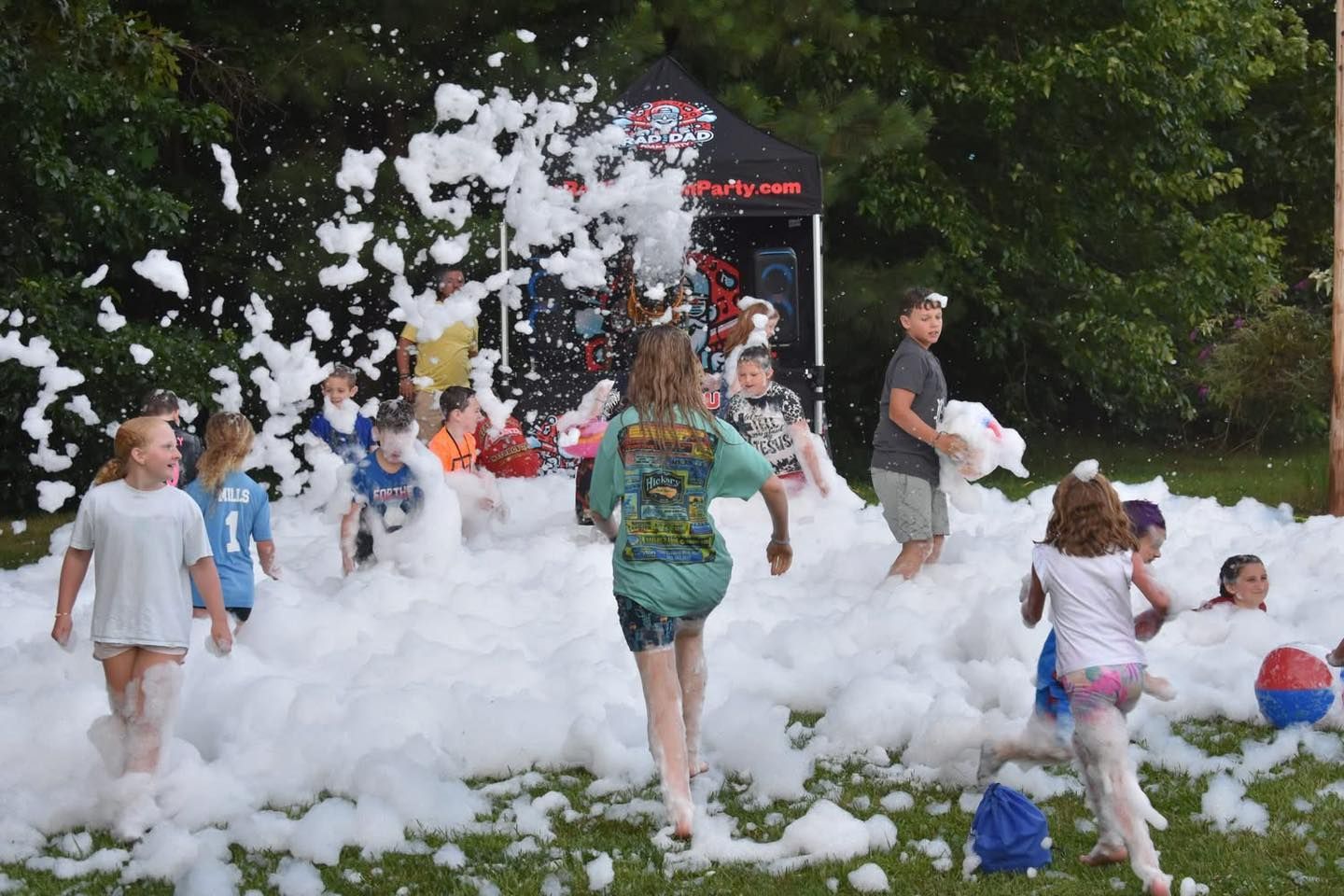 Children playing in a foam-filled park, with bubbles flying around a small kiosk.