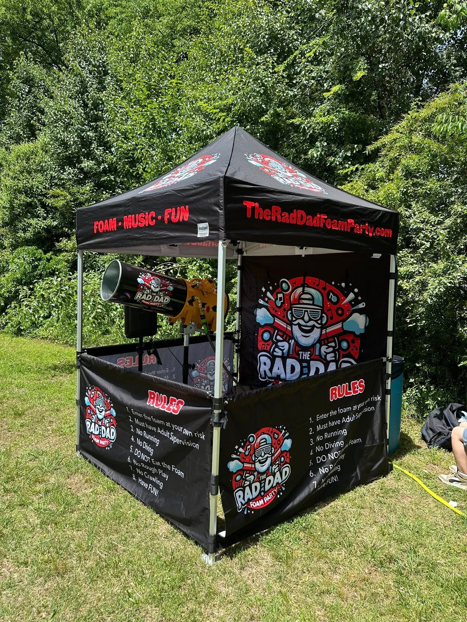 Black and red pop-up tent with band logos on a grassy lawn by trees