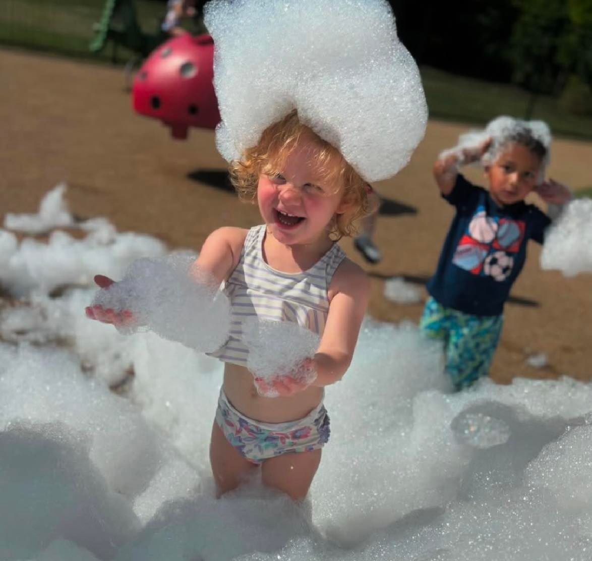 Children playing in foam outdoors, smiling and covered in bubbles.