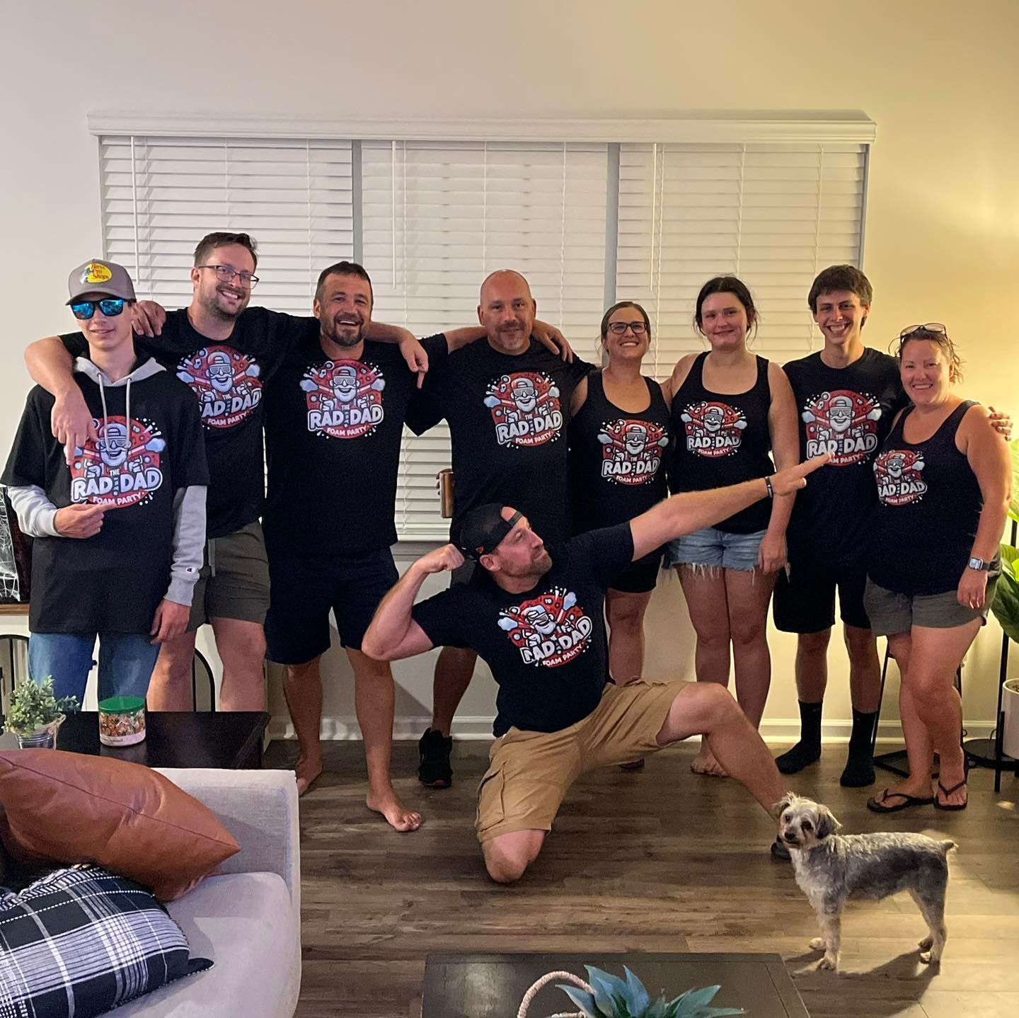 Group of people posing indoors in matching black shirts, with one kneeling playfully in front.