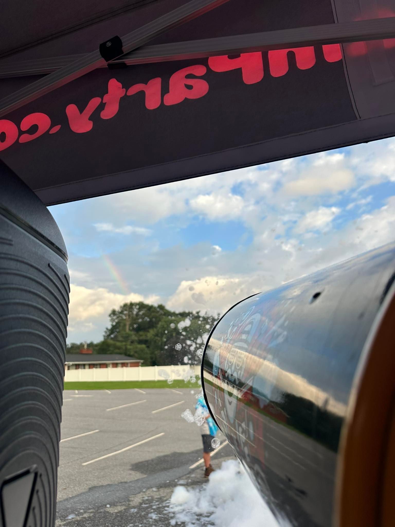 View from inside a vehicle through a windshield at a parking lot and cloudy sky, with red lettering overhead.