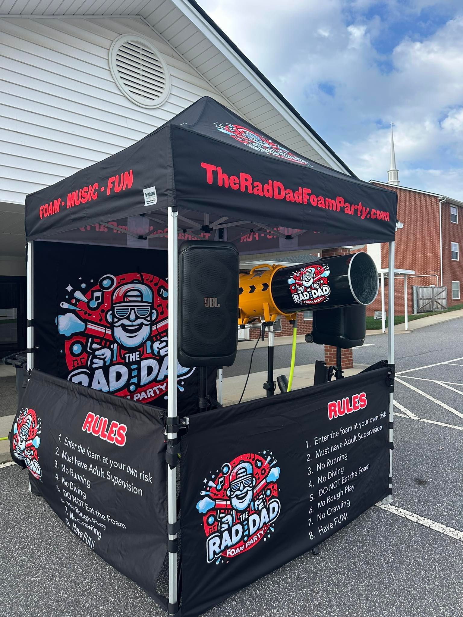 Black food kiosk with red-and-white branding and a hot dog grill outside a brick building.