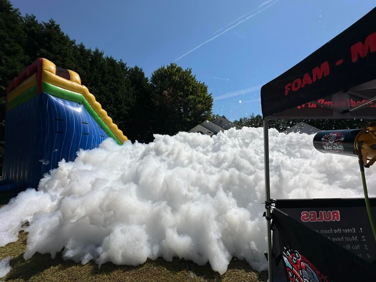 Foam party with a giant white foam pile beside a blue-and-yellow inflatable slide and canopy tent