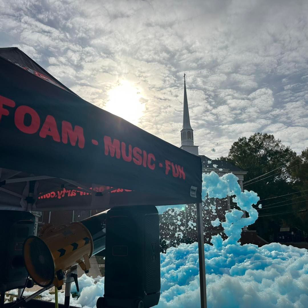 Foam party stage with blue foam, music speakers, and a church steeple at sunset