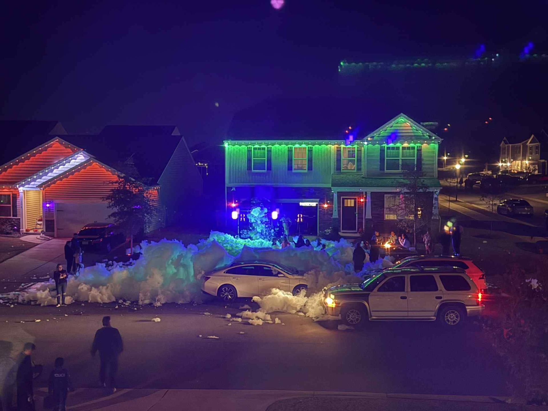 Nighttime fire scene with flashing emergency lights outside a decorated two-story house and parked vehicles