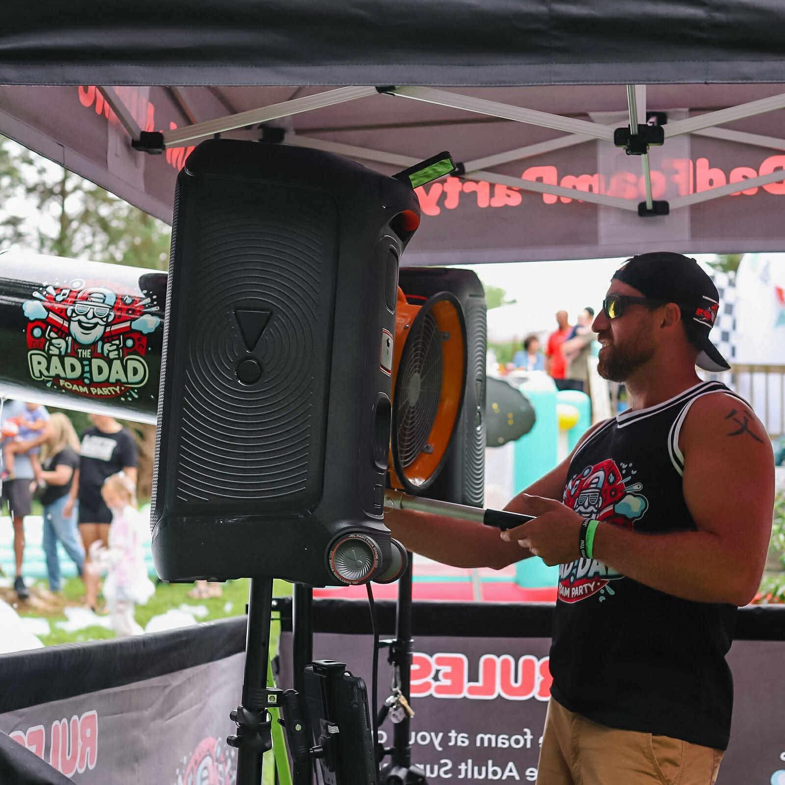 Man performing on a drum pad beside a large speaker under a tent at an outdoor event
