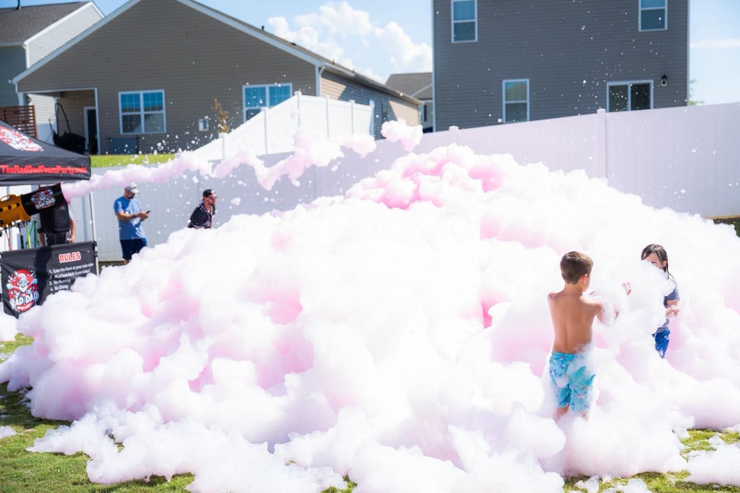 Children play in a huge pink-and-white foam pile at an outdoor neighborhood event.