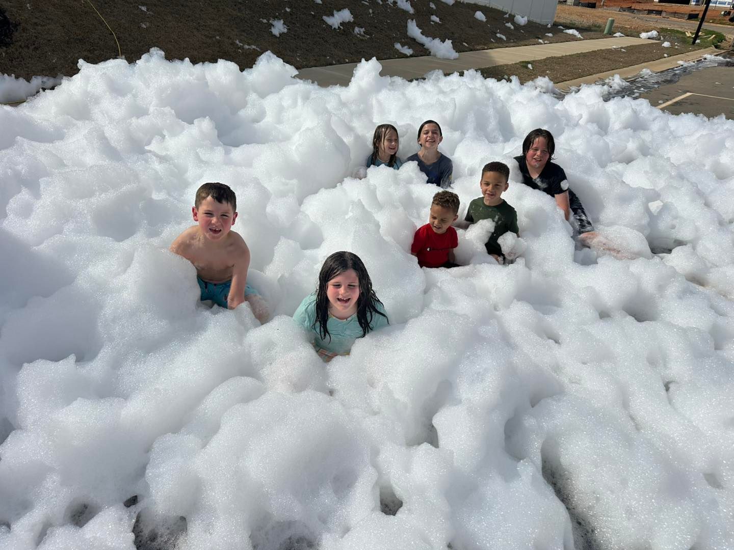 Children playing in a large pile of white foam outdoors, smiling and half-buried