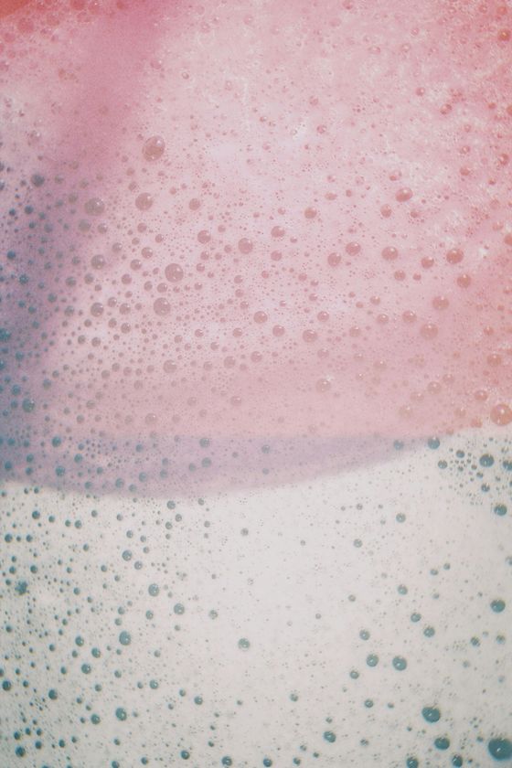 Pink and white bubbly foam with scattered blue-gray bubbles, like a close-up of soap suds