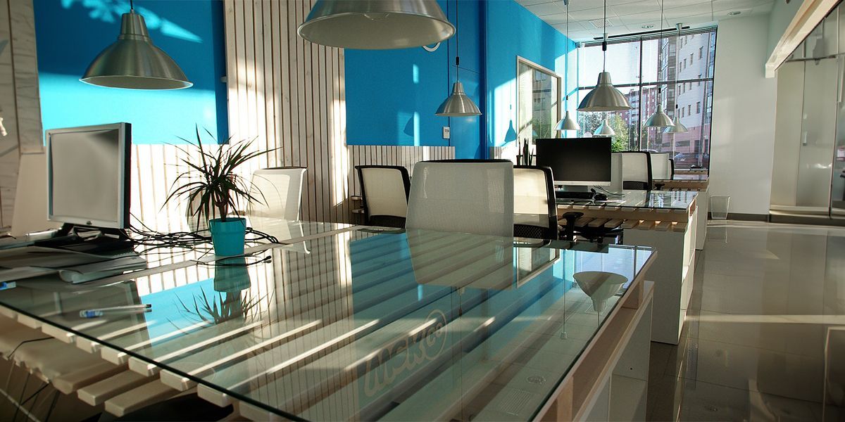 Modern office interior with blue walls, glass table, and sunlight.