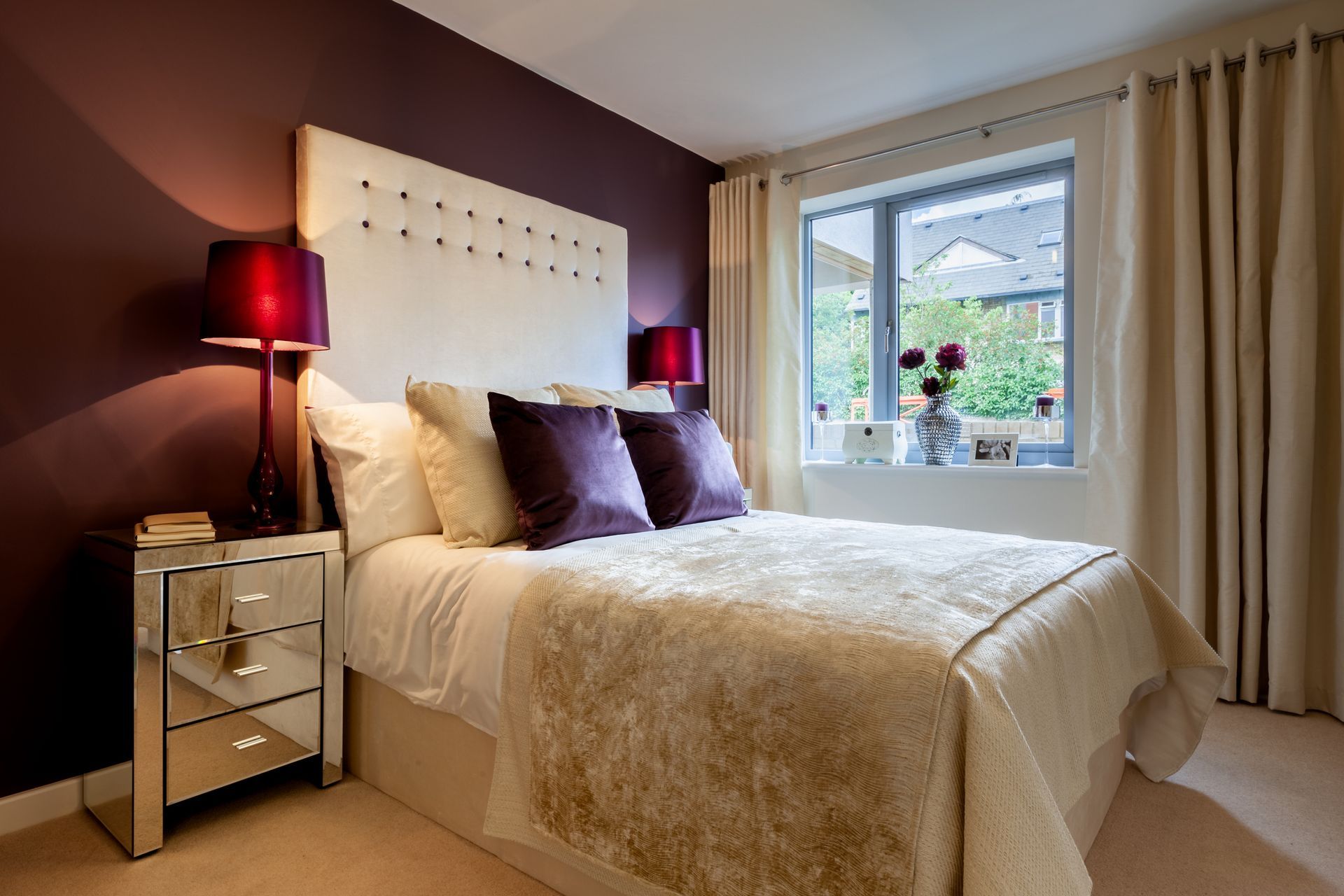 Bedroom with purple accent wall, mirrored nightstand, and ivory bedding.