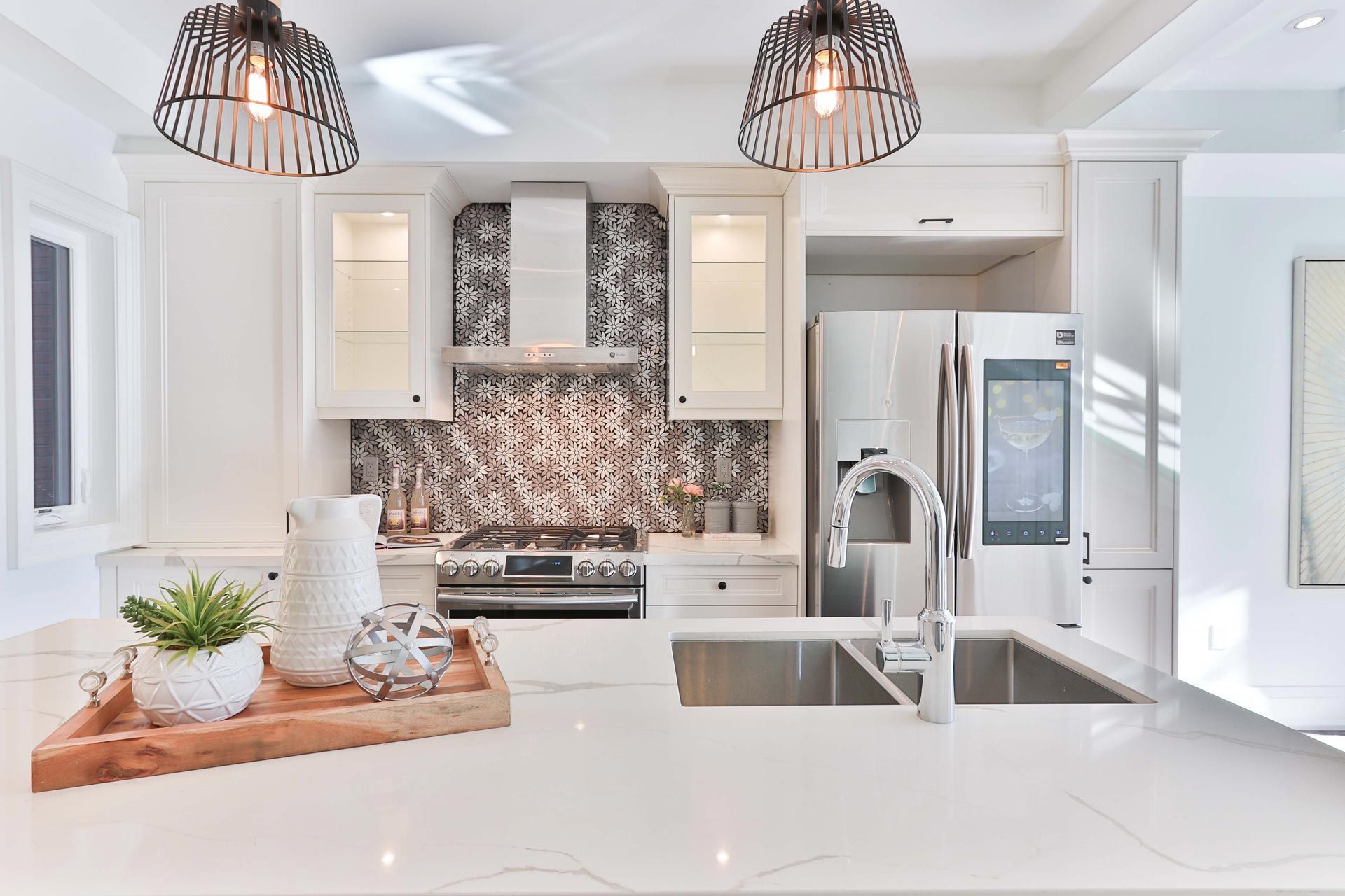 Bright white kitchen with stainless steel appliances, patterned backsplash, and modern lighting.