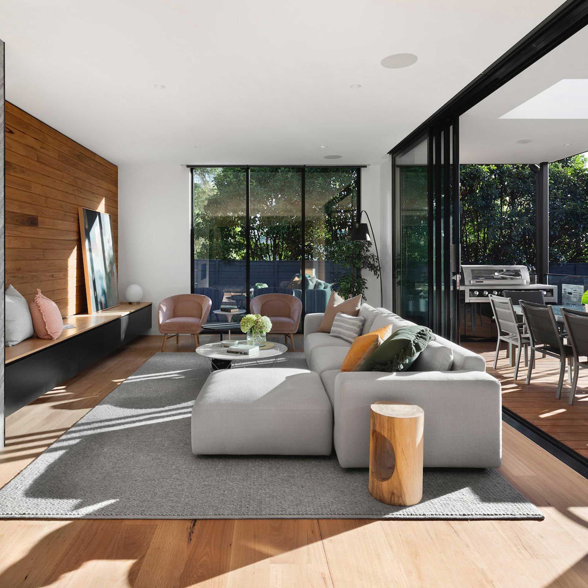 Modern living room with light-colored sofa, wooden accent wall, and sliding glass doors to an outdoor dining area.