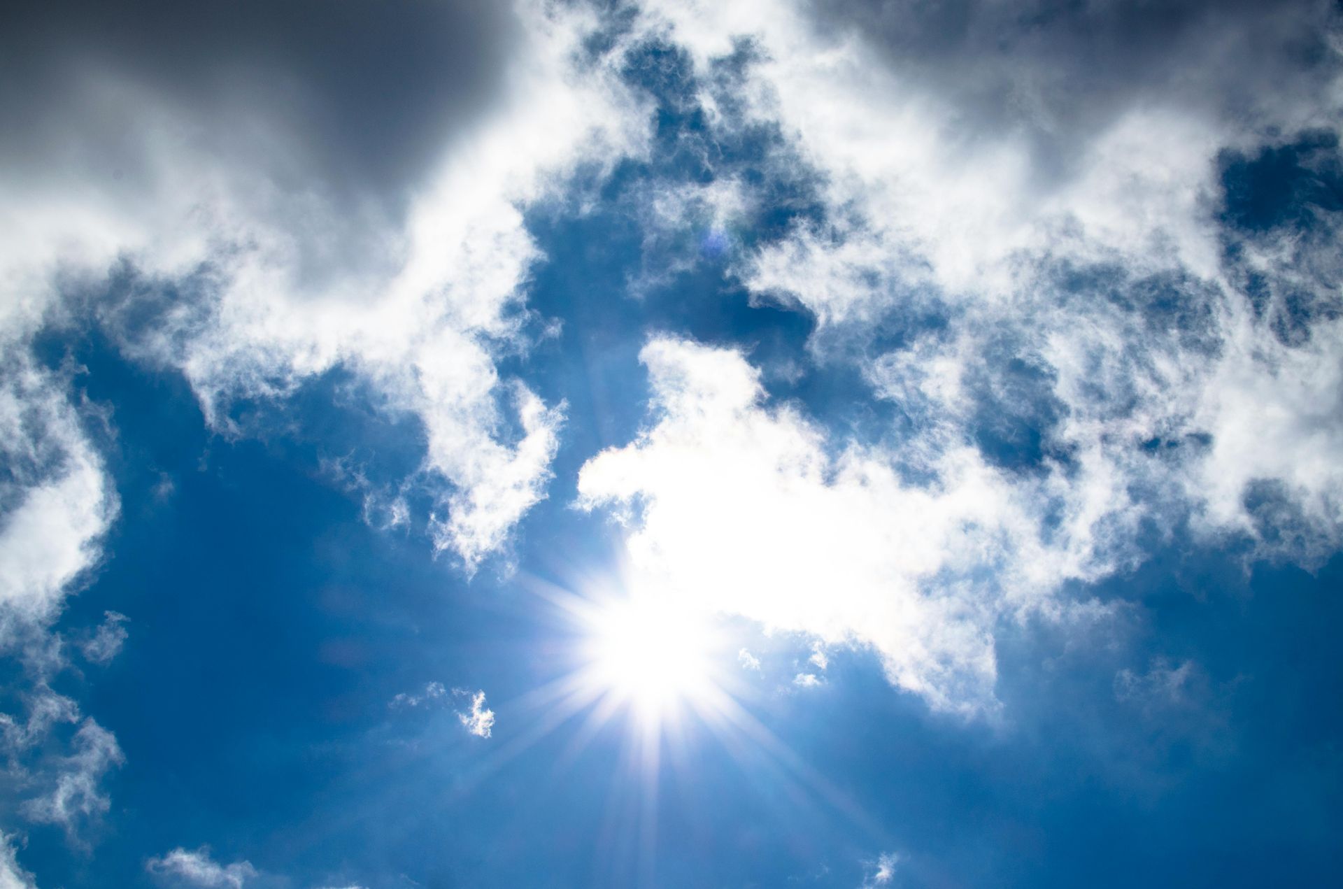 Bright sun shining through white clouds in a clear blue sky.