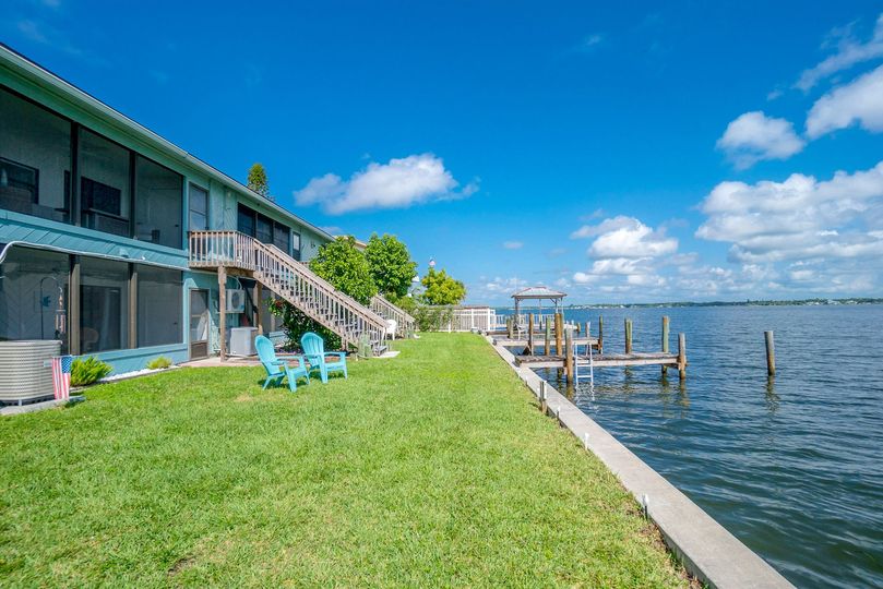 A house with a dock and chairs in front of it next to a body of water.