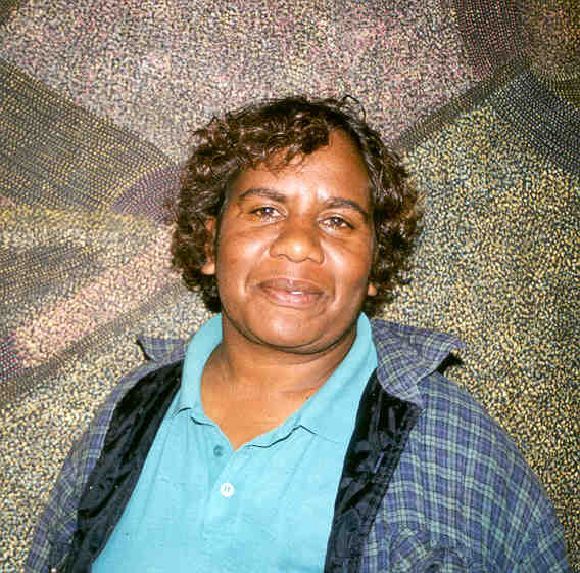 A woman with curly hair is wearing a blue shirt and plaid jacket