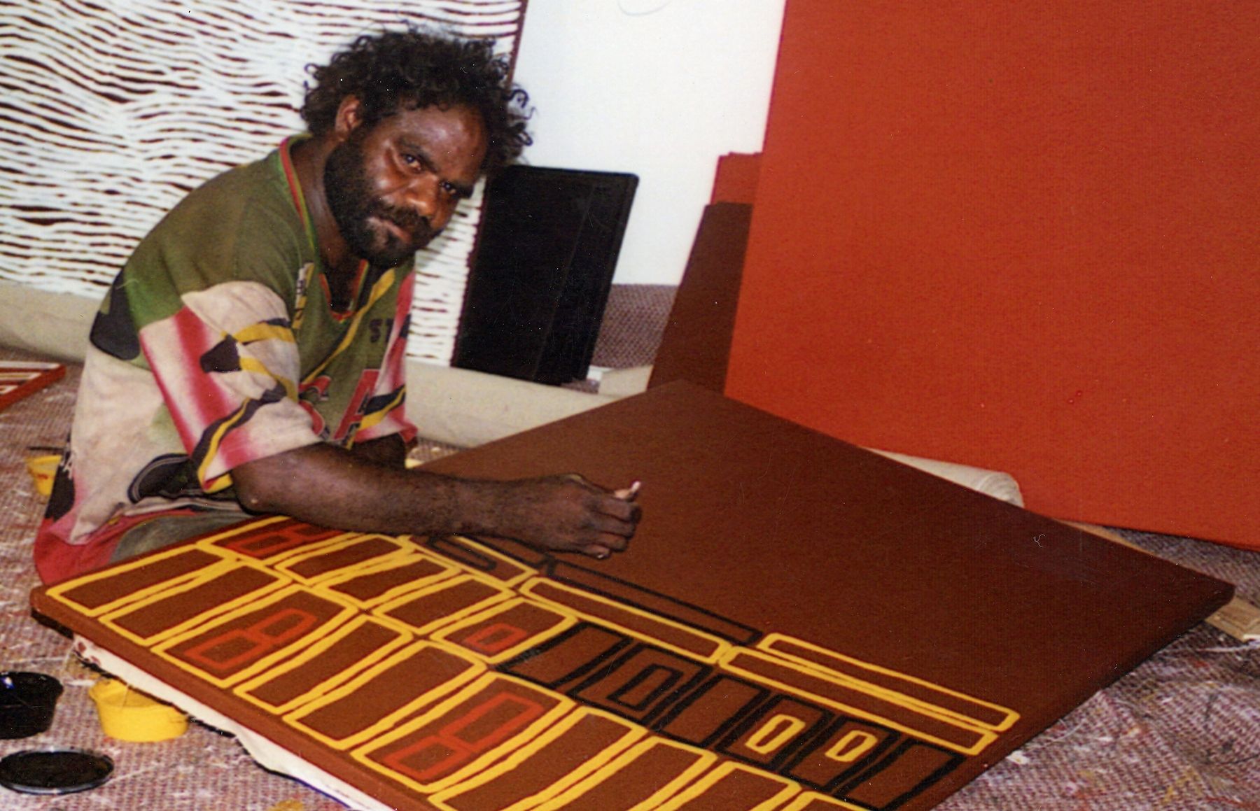 A man is sitting on the floor painting a large piece of art