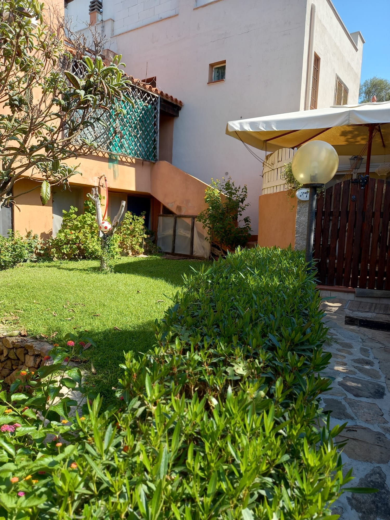 Giardino lussureggiante con arbusti, erba e un edificio con muri e scale arancioni.