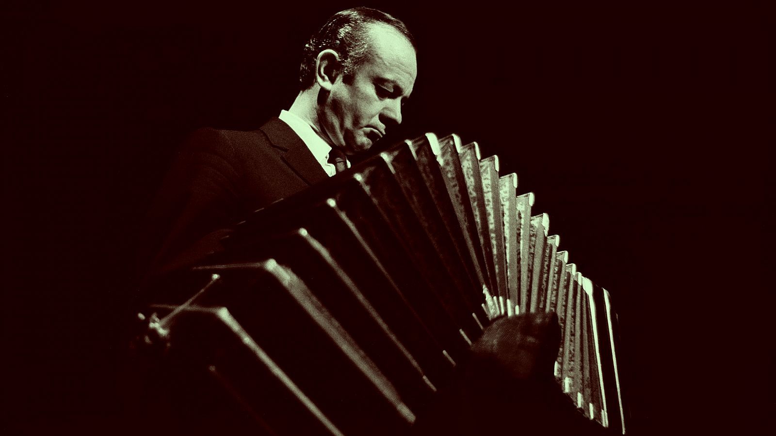 Hombre tocando un bandoneón (instrumento parecido al acordeón) en condiciones de poca luz.