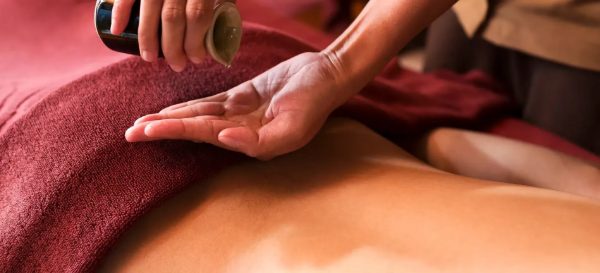 Massage therapist using a wooden tool on a person’s back, covered with a red towel