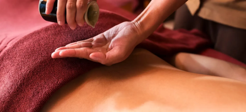 Massage therapist using a wooden tool on a person’s back, covered with a red towel